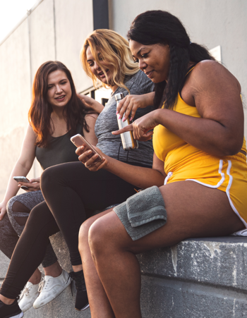 A group of 3 women socialising with eachother outside looking at one of their phones