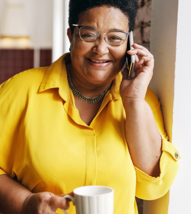 Lady talking on her phone holding a cup of tea and wearing a bright yellow shirt
